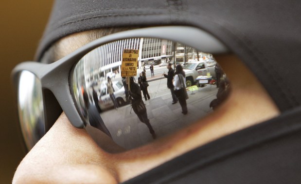 V okuliaroch policajta sa odráža  demonštrant s heslom kapitalizmus je organizovaný zločin